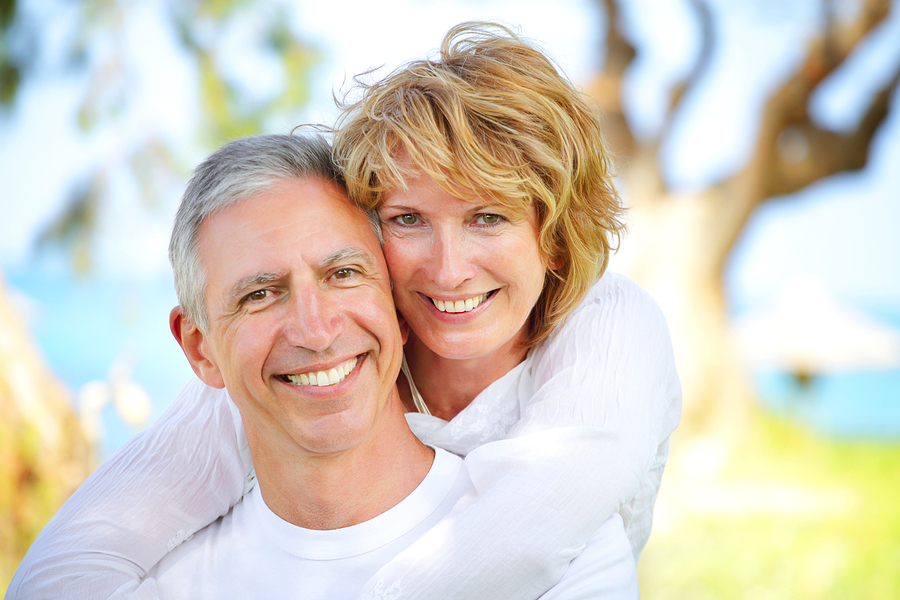middle aged couple hugging smiling outdoors near trees and lake, Windsor Locks, CT veneers